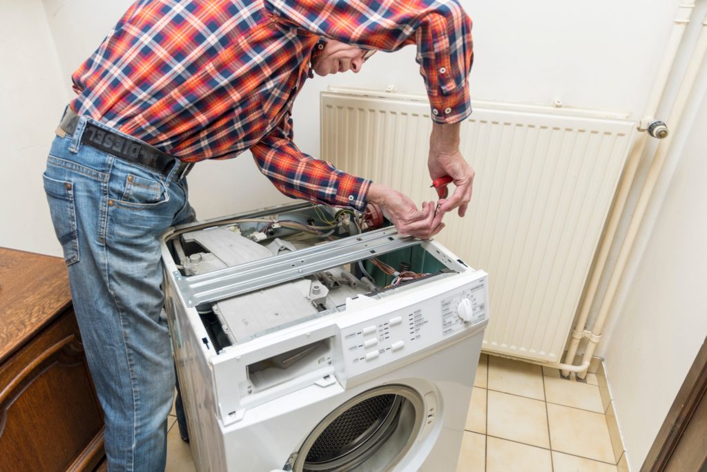 Middle aged man repairing broken washing machine with tools, household chores