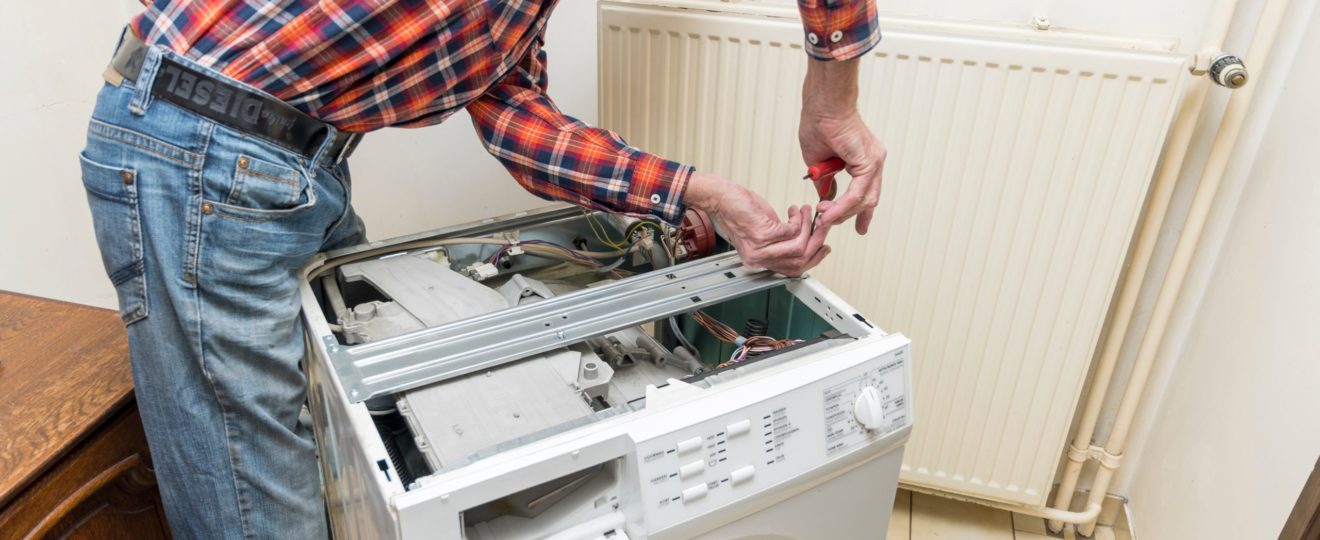 Middle aged man repairing broken washing machine with tools, household chores