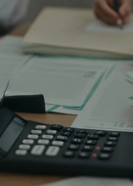 a person sitting at a desk with a calculator and a stack of financial documents.